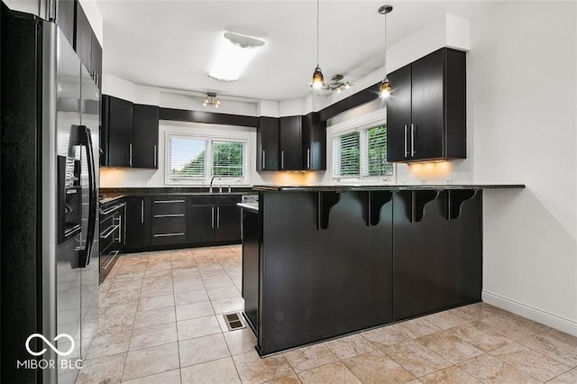 kitchen featuring black range oven, stainless steel fridge, hanging light fixtures, kitchen peninsula, and a kitchen bar