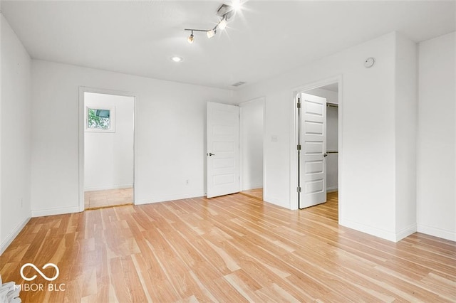 unfurnished bedroom featuring a spacious closet, a closet, and light hardwood / wood-style flooring