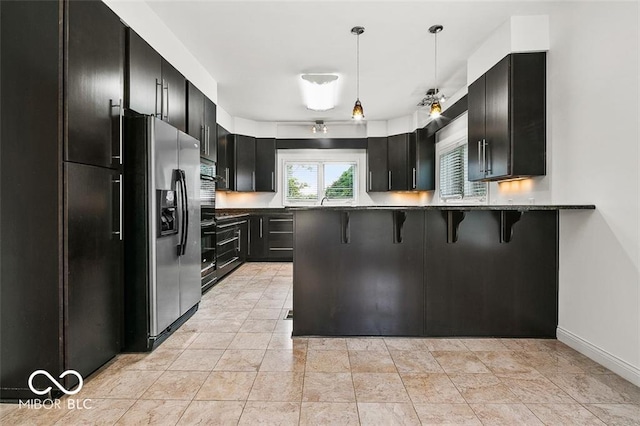 kitchen featuring pendant lighting, dark stone counters, kitchen peninsula, a kitchen breakfast bar, and stainless steel fridge