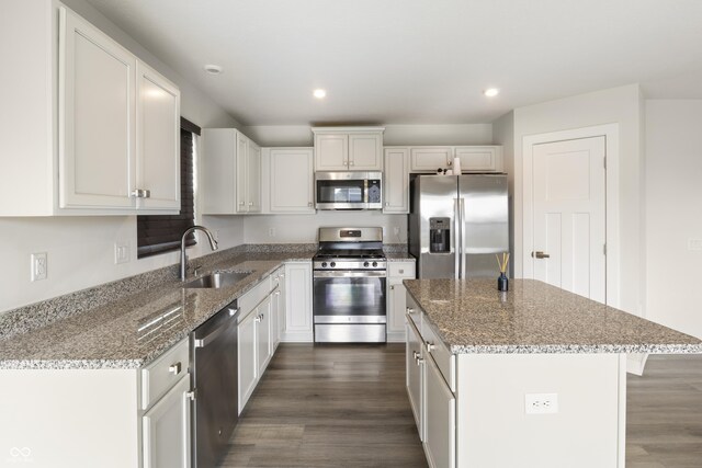 kitchen featuring stainless steel appliances, sink, light stone countertops, dark hardwood / wood-style flooring, and a kitchen island