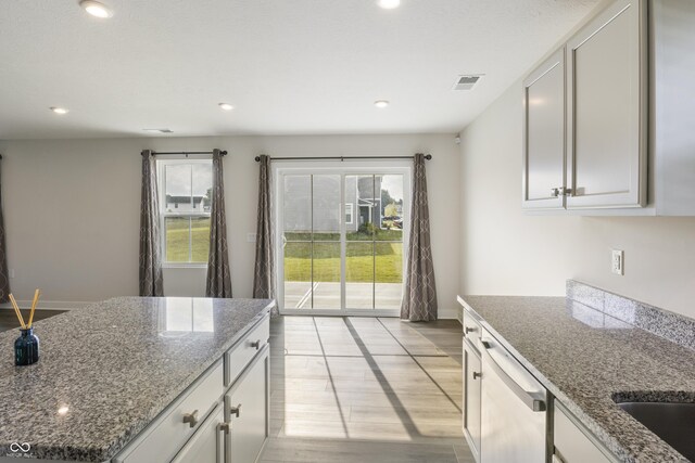 kitchen with white cabinetry, light hardwood / wood-style flooring, stone countertops, and dishwasher