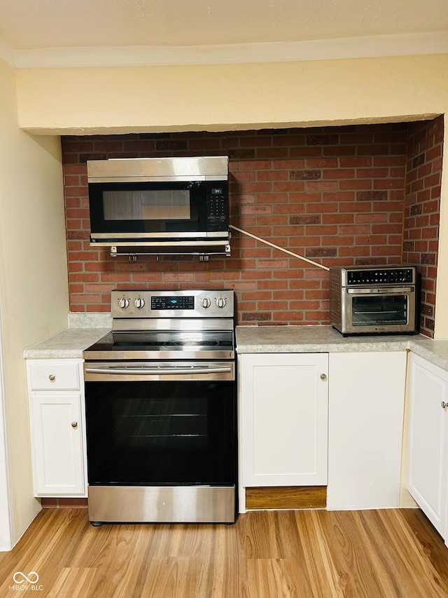 kitchen featuring white cabinetry, light hardwood / wood-style flooring, crown molding, and appliances with stainless steel finishes