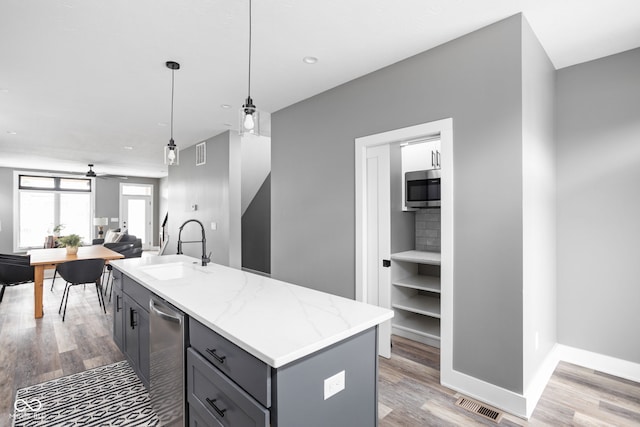 kitchen with decorative light fixtures, light stone countertops, a center island with sink, light hardwood / wood-style floors, and sink