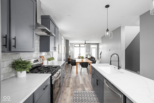 kitchen with gray cabinetry, decorative light fixtures, appliances with stainless steel finishes, sink, and wall chimney range hood