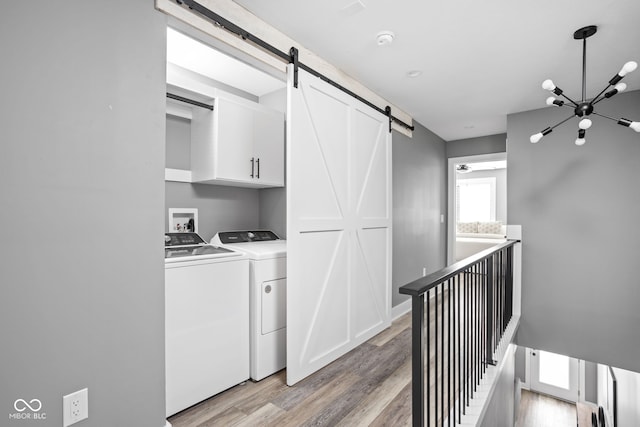 clothes washing area with light wood-type flooring, a notable chandelier, independent washer and dryer, and a barn door