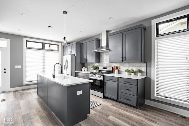 kitchen with a center island with sink, stainless steel appliances, wall chimney exhaust hood, and a healthy amount of sunlight