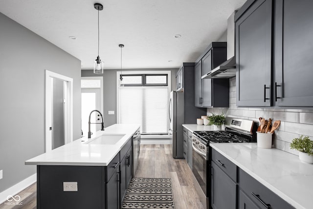 kitchen featuring decorative light fixtures, stainless steel appliances, sink, a center island with sink, and tasteful backsplash