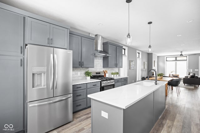 kitchen featuring hanging light fixtures, stainless steel appliances, gray cabinets, and wall chimney range hood