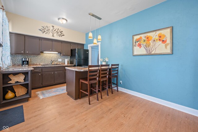 kitchen featuring light wood-type flooring, tasteful backsplash, light stone countertops, a breakfast bar area, and black refrigerator