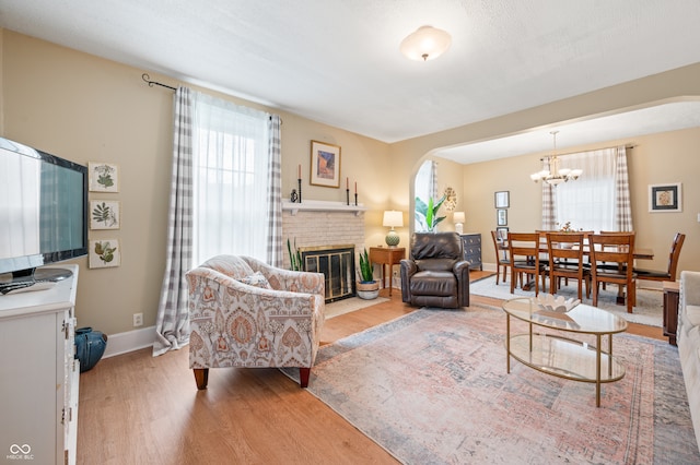 living room with a notable chandelier, a brick fireplace, and light hardwood / wood-style floors