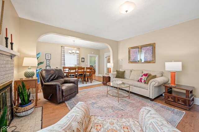 living room with a notable chandelier, wood-type flooring, and a brick fireplace