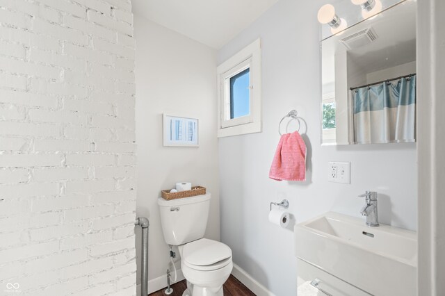 bathroom featuring hardwood / wood-style flooring, toilet, brick wall, and vanity