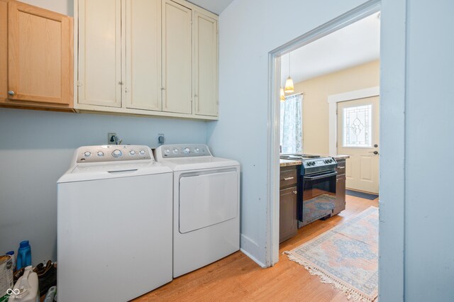 clothes washing area with separate washer and dryer, light hardwood / wood-style flooring, and cabinets