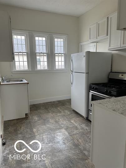 kitchen with light tile patterned flooring, sink, light stone counters, stainless steel gas range, and white cabinetry