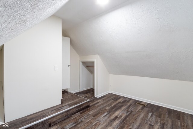 additional living space with a textured ceiling, lofted ceiling, and dark wood-type flooring