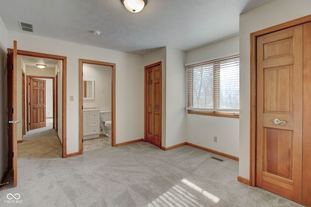 unfurnished bedroom featuring a textured ceiling, light colored carpet, ensuite bath, and a closet