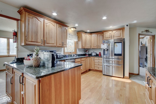 kitchen with appliances with stainless steel finishes, dark stone countertops, sink, and light hardwood / wood-style flooring