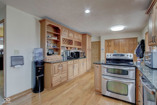 kitchen with dark stone countertops, appliances with stainless steel finishes, and light hardwood / wood-style flooring