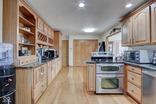 kitchen featuring appliances with stainless steel finishes, dark stone countertops, light hardwood / wood-style floors, and a textured ceiling