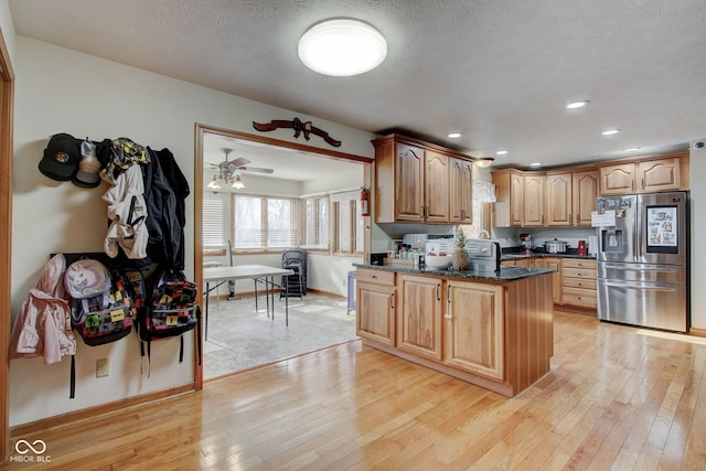 kitchen featuring a textured ceiling, stainless steel fridge, ceiling fan, dark stone countertops, and light wood-type flooring