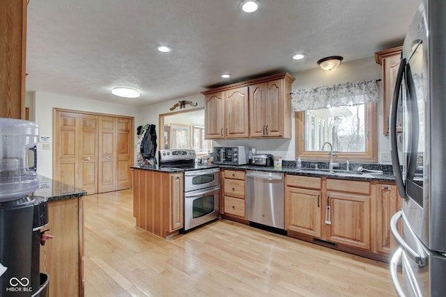 kitchen with dark stone countertops, appliances with stainless steel finishes, light hardwood / wood-style floors, sink, and a textured ceiling