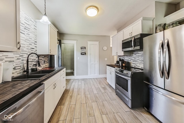 kitchen featuring sink, appliances with stainless steel finishes, decorative backsplash, white cabinetry, and hanging light fixtures