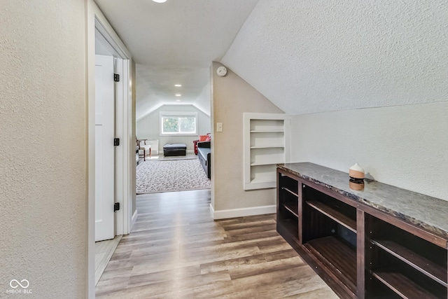 corridor featuring built in shelves, a textured ceiling, lofted ceiling, and wood-type flooring