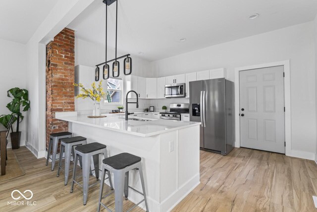 1046 Dawson St, Indianapolis, IN 46203 - kitchen with a kitchen bar, light wood-type flooring, stainless steel appliances, a sink, and white cabinets