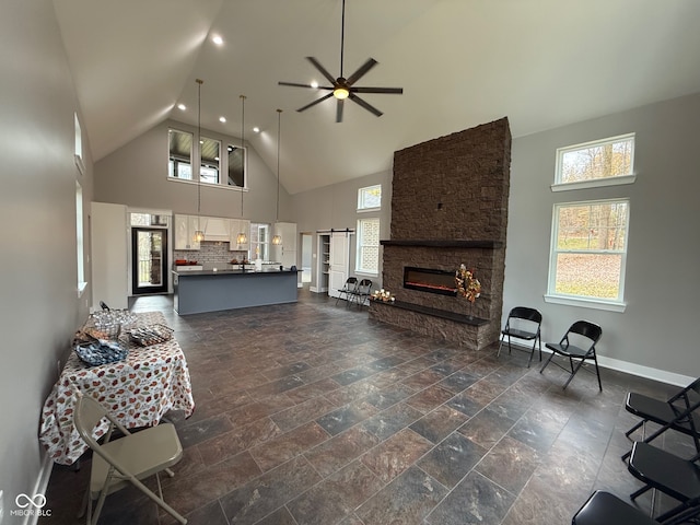 living room with ceiling fan, a barn door, a stone fireplace, and high vaulted ceiling