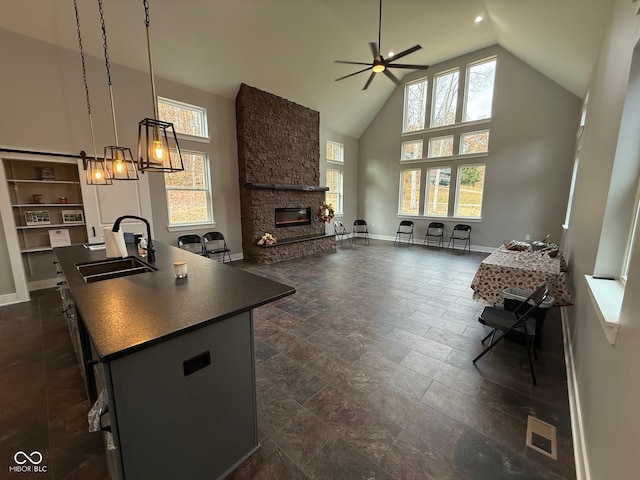 kitchen with a kitchen island with sink, high vaulted ceiling, sink, hanging light fixtures, and a fireplace