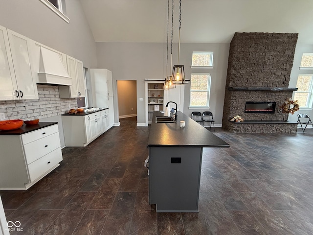 kitchen featuring custom range hood, a kitchen island with sink, sink, pendant lighting, and dark hardwood / wood-style floors