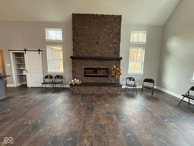 unfurnished living room featuring a fireplace, a towering ceiling, a barn door, and plenty of natural light