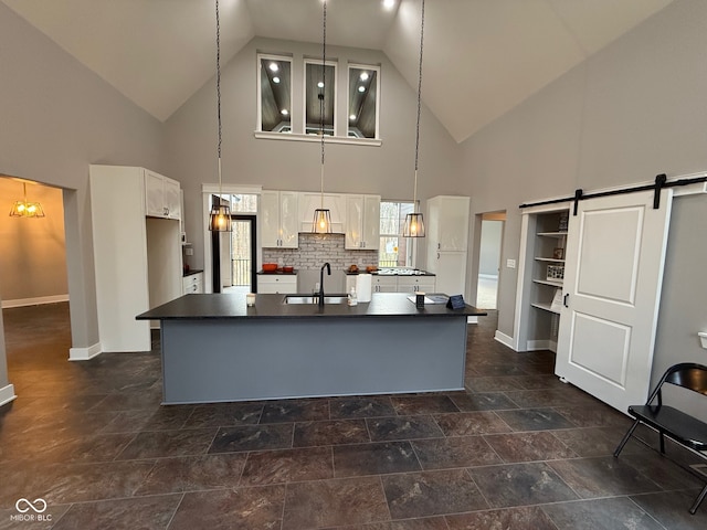 kitchen with a kitchen island with sink, high vaulted ceiling, sink, a barn door, and decorative light fixtures