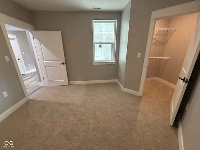 unfurnished bedroom with a walk in closet, a closet, and light colored carpet