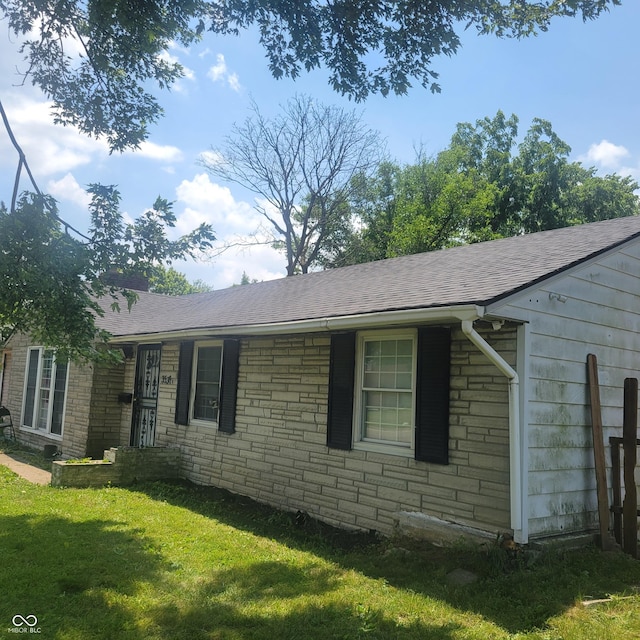 view of side of property with a shingled roof, stone siding, and a yard