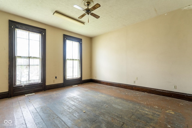 empty room with a ceiling fan, wood-type flooring, a textured ceiling, and baseboards