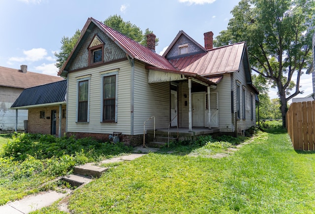 victorian house with a standing seam roof, metal roof, fence, a chimney, and a front yard