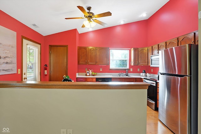 kitchen featuring vaulted ceiling, appliances with stainless steel finishes, sink, ceiling fan, and light wood-type flooring