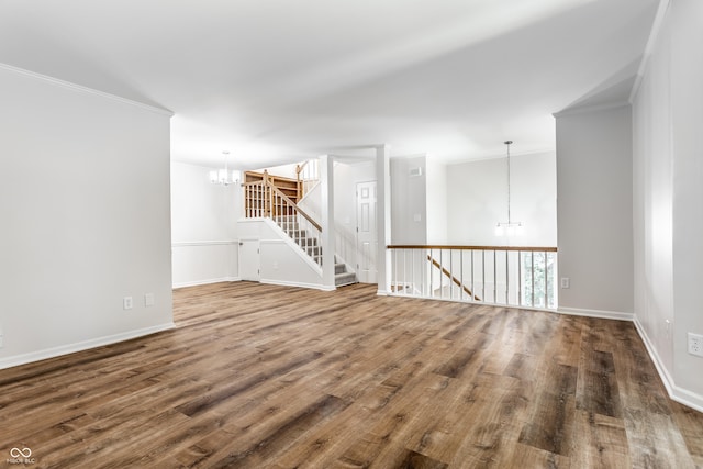 empty room with wood finished floors, crown molding, baseboards, a chandelier, and stairs