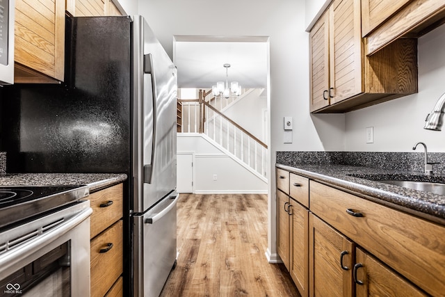 kitchen with light wood-type flooring, freestanding refrigerator, brown cabinetry, a notable chandelier, and a sink