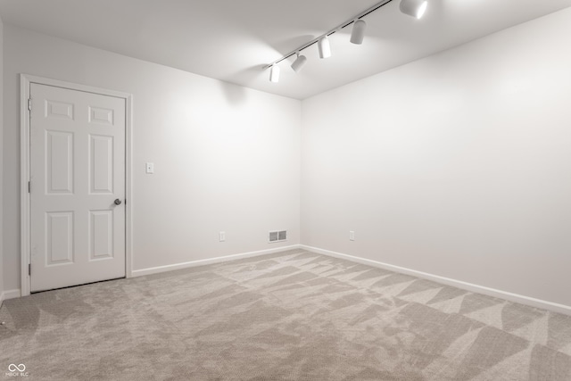 spare room with visible vents, carpet flooring, track lighting, and baseboards