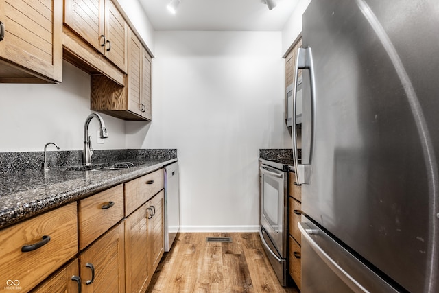 kitchen featuring dark stone countertops, wood finished floors, baseboards, a sink, and appliances with stainless steel finishes