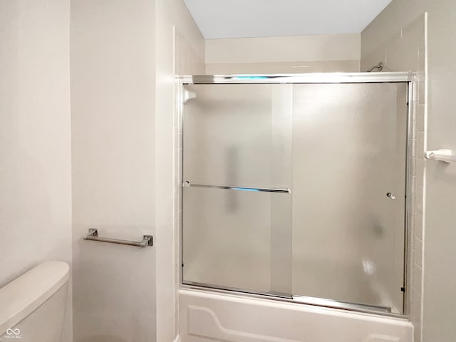 bathroom featuring toilet and bath / shower combo with glass door