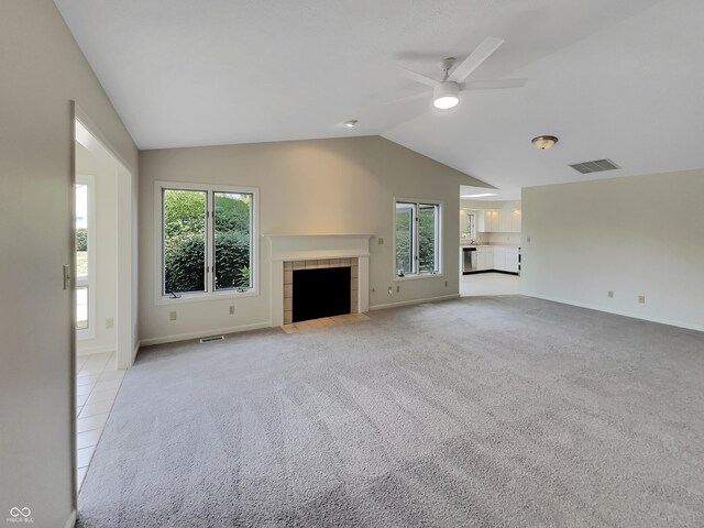 unfurnished living room with plenty of natural light, lofted ceiling, light carpet, and a tile fireplace