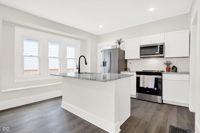 kitchen with appliances with stainless steel finishes, white cabinetry, dark wood-type flooring, light stone countertops, and a center island with sink