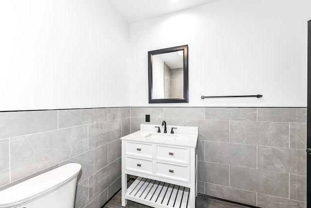 bathroom featuring vanity, tile walls, toilet, and a wainscoted wall