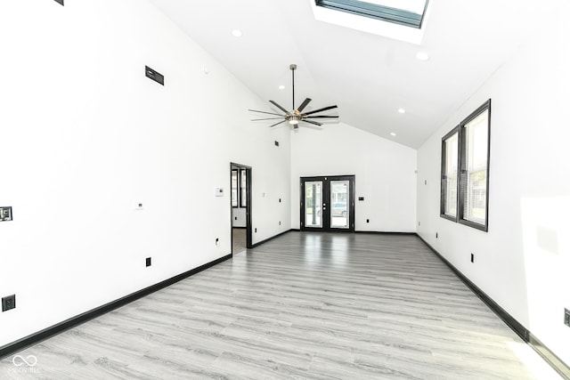 unfurnished room with baseboards, high vaulted ceiling, a skylight, french doors, and light wood-style floors