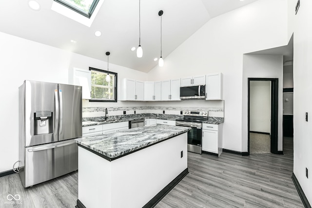 kitchen featuring dark stone countertops, a skylight, appliances with stainless steel finishes, white cabinetry, and decorative light fixtures