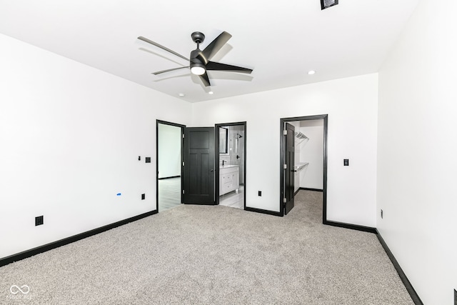 unfurnished bedroom with light carpet, a ceiling fan, ensuite bathroom, baseboards, and a spacious closet