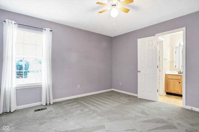 unfurnished bedroom with ceiling fan, light colored carpet, sink, and ensuite bath